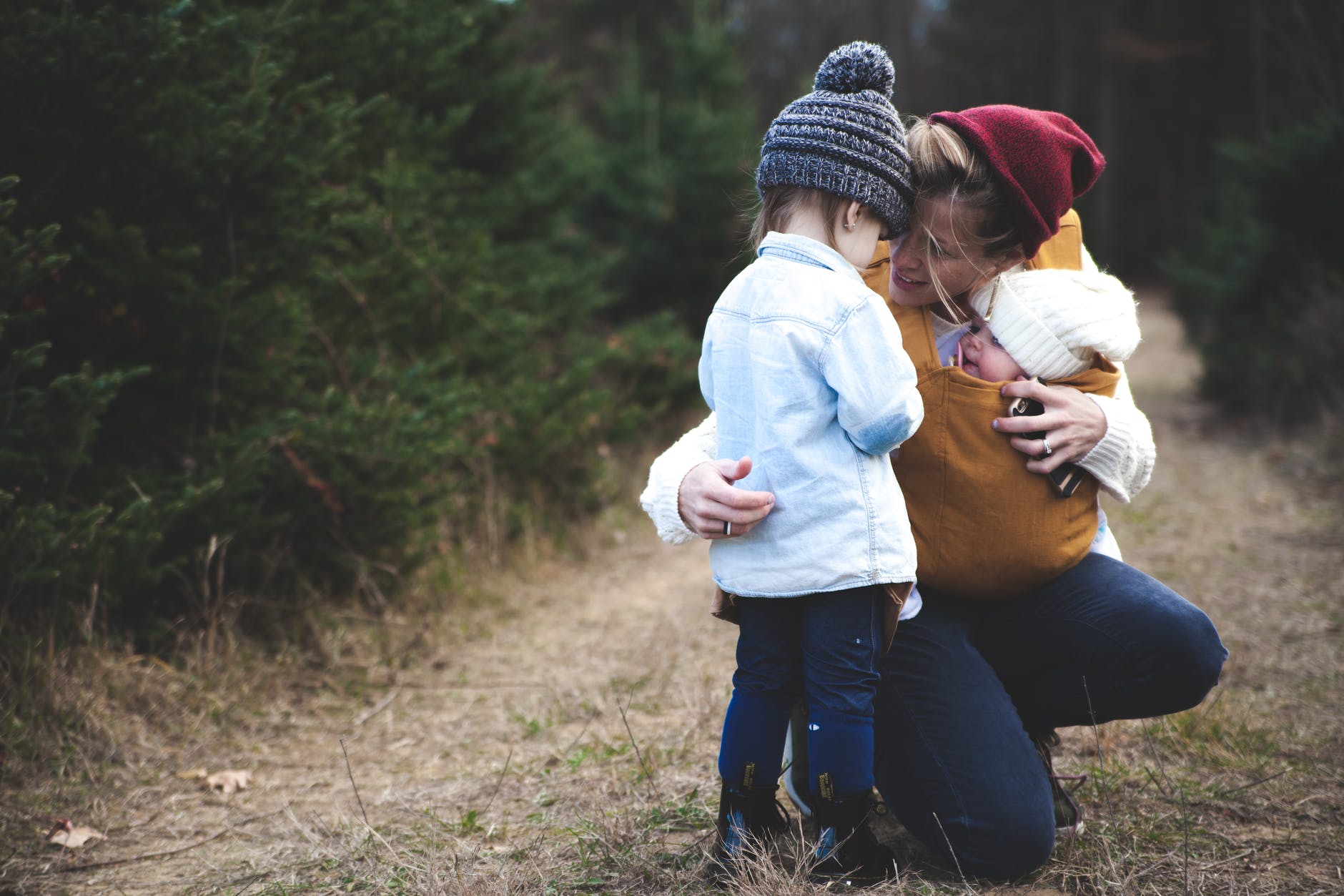 A woman outside hugging her two young children. Photo by Josh Willink on Pexels.com.